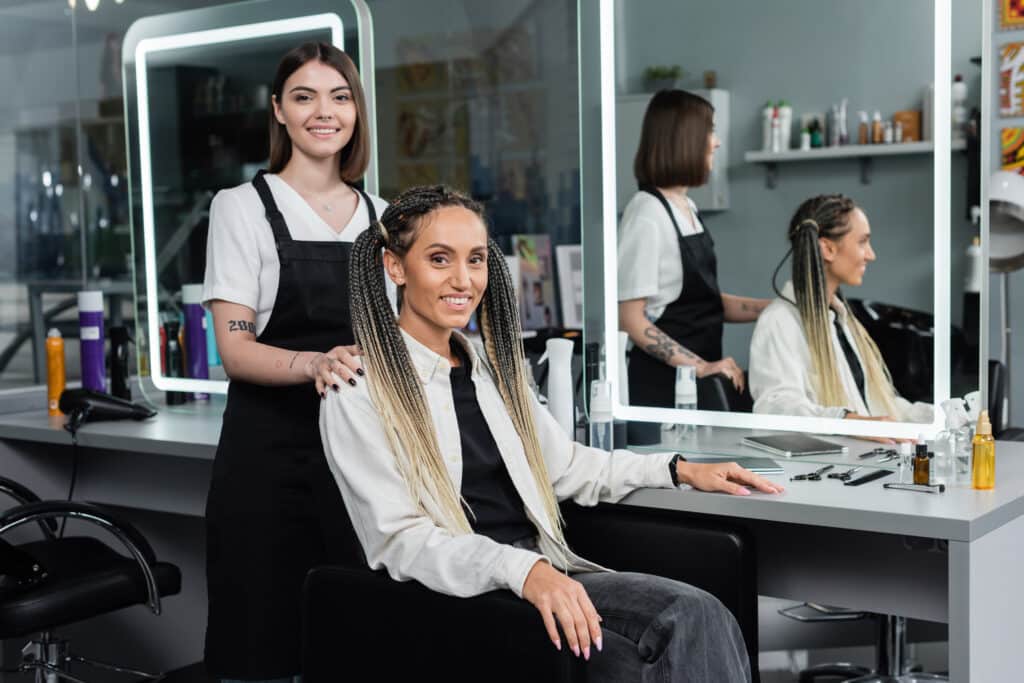 hairdresser and female client beauty salon cheerful woman with braids and two ponytails smiling