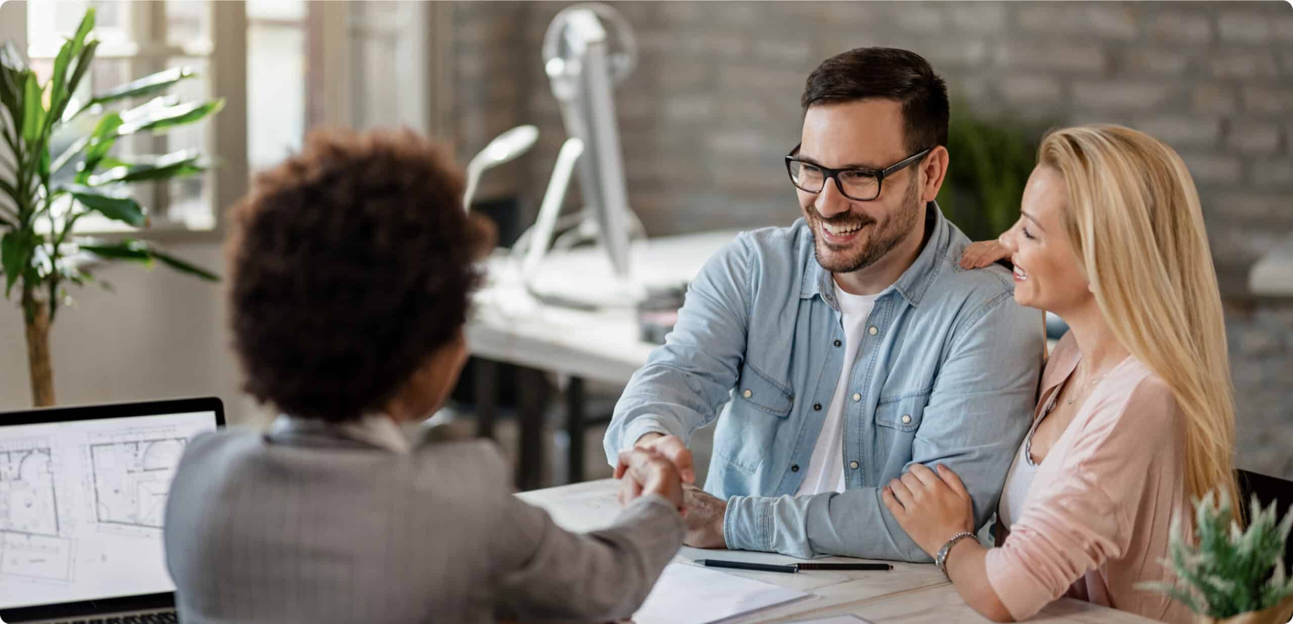 happy couple handshaking with financial advisor meeting office focus is man